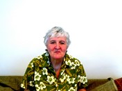 Katherine Barrett is a RAP member. She is a white woman with grey hair, sitting on her sofa. She wears a bright green blouses with white flowers on it.